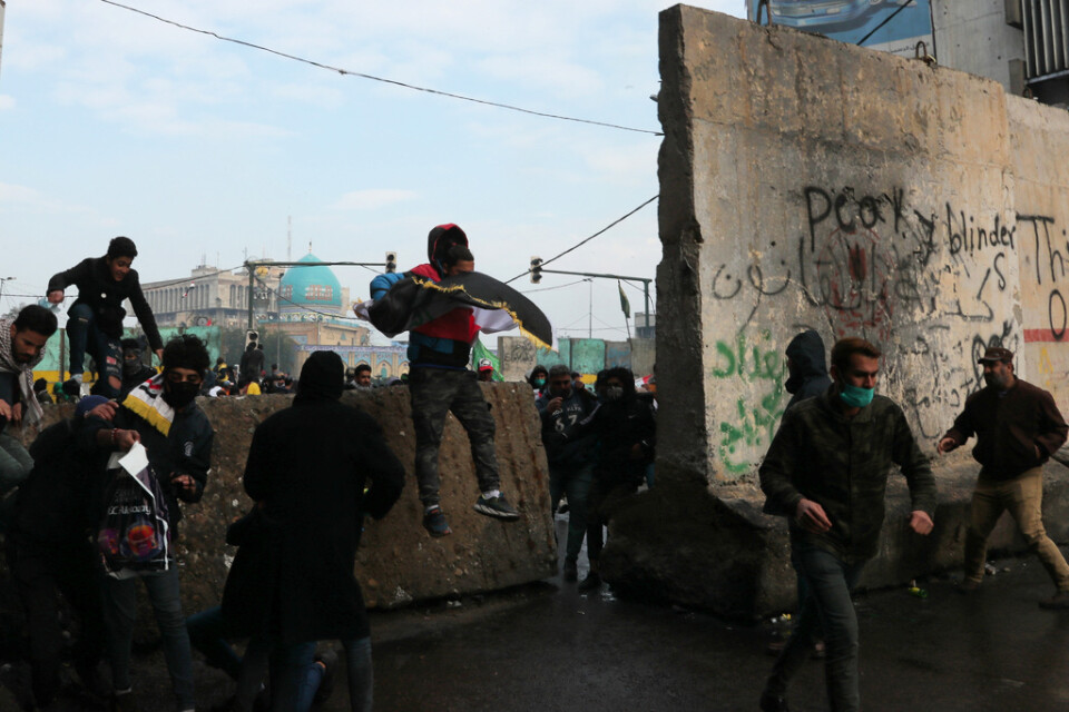 Regeringskritiska demonstranter tar skydd bakom betongavspärrningar i Bagdad under sammandrabbningar med säkerhetsstyrkor.