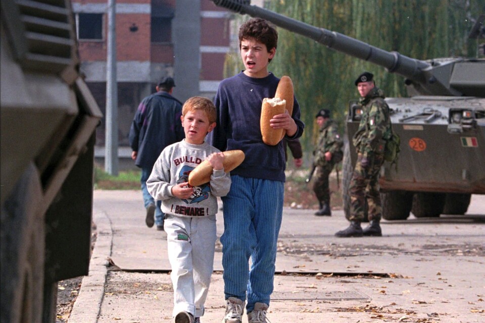 Två pojkar promenerar i Sarajevo med en italiensk NATO-fredstrupp bakom sig.