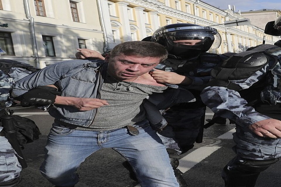 Poliser griper en demonstrant under lördagens regimkritiska protester i Moskva.