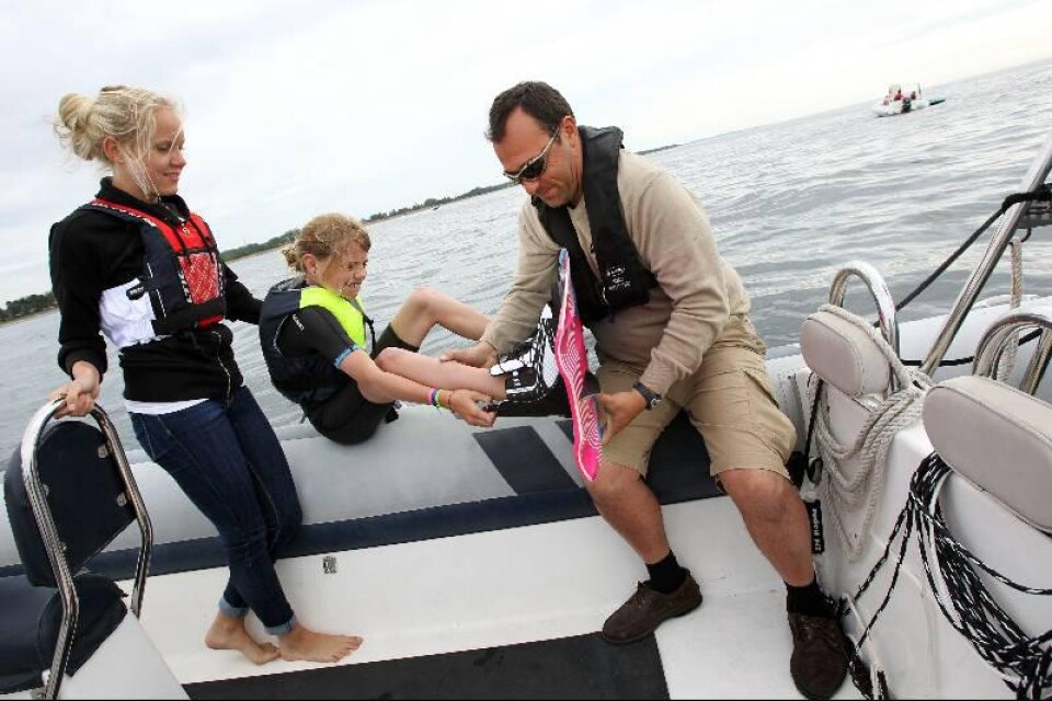 Instruktörerna Hilma Nilsson och Henrik de Vries hjälper 10-åriga Hilma Ivarsson att få in fötterna i wakeboarden.