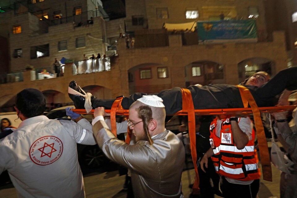 Israeliska sjukvårdare och en ung man bär i väg en man som skadats när en läktare rasade i en synagoga invid Jerusalem på lördagen.