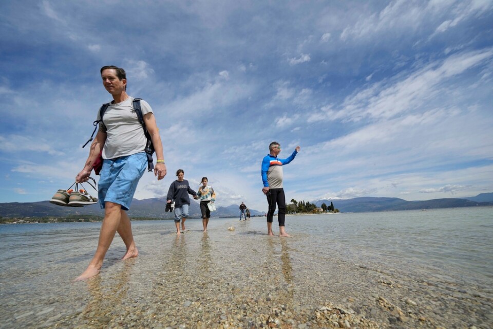 Turister promenerar från fastlandet till ön San Biagio i Gardasjön.
