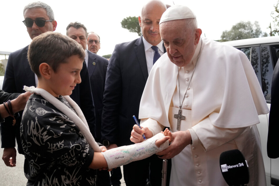 Påve Franciskus signerar en pojkes gips i samband med att han lämnar sjukhuset på lördagsförmiddagen.