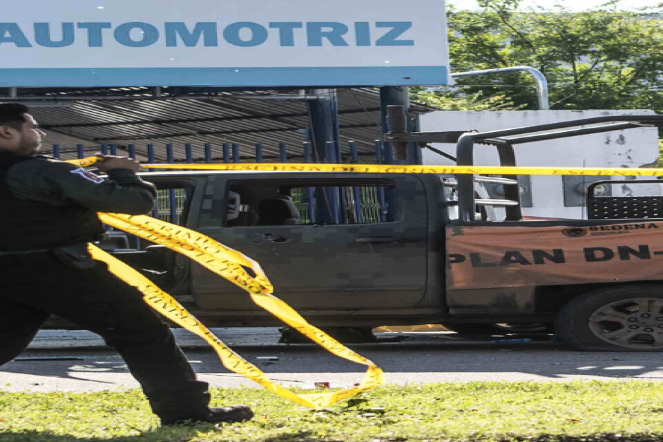 En mexikansk polis spärrar av platsen där ett av säkerhetsstyrkornas sönderskjutna fordon står.