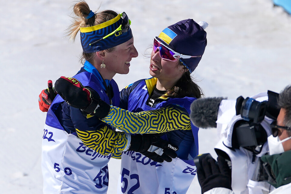 Guldmedaljören Iryna Bui, till höger, kramar om Oleksandra Kononova, vänster efter att de vann guld- och silvermedalj i damernas medeldistanslopp i skidskytte.