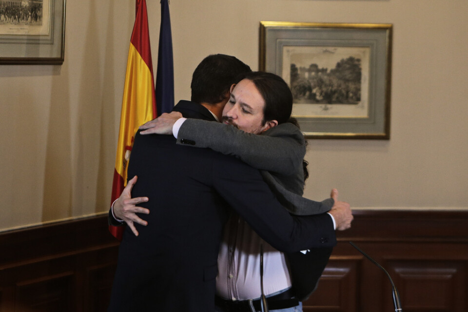 Spaniens tillförordnade premiärminister Pedro Sánchez (tv) kramas med Unidas Podemos-ledaren Pablo Iglesias efter att ha skrivit under en pakt om att bilda en koalitionsregering.