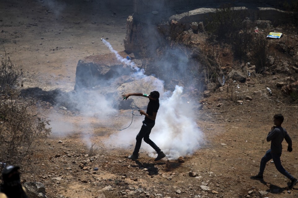 En palestinsk demonstrant kastar tillbaka en tårgasbehållare som israelisk militär använt vid protester mot bosättningen i Eviatar. Bild från tidigare i juli.