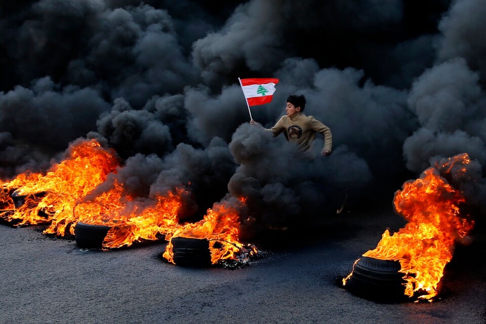 En bild från tisdagens våldsamma protester i Beirut, riktade mot regeringen i Libanon. En pojke ses hoppa på utplacerade brinnande bildäck.