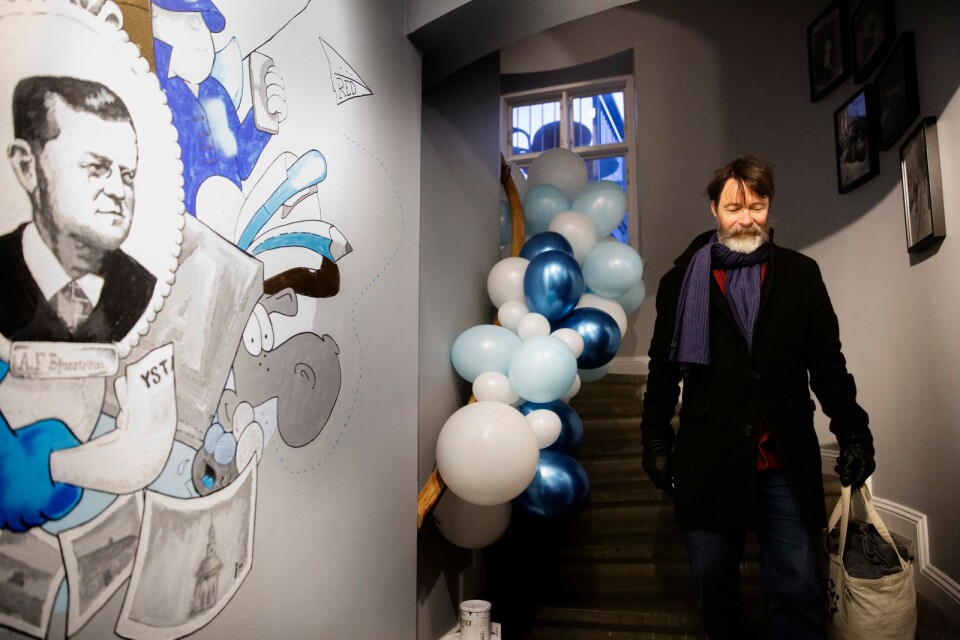 Kulturredaktör Ulf Mårtensson i trappan på det nya tidningshuset, med en sprillans ny väggmålning föreställande YA:s grundare Axel Fredrik Bjurström.
