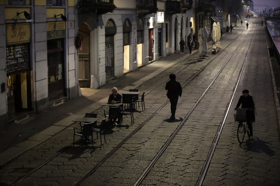 En man sitter ensam utanför en bar i Milano. Det rapporteras ha varit ovanligt stillsamt i storstaden med anledning av virusspridningen.