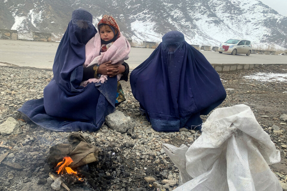 Två kvinnor och en 1,5 år gammal pojke värmer sig vid en brasa i östra Afghanistan i januari 2022.