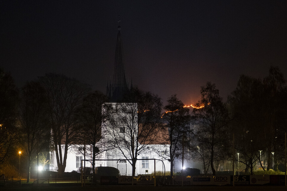 Det brinner på tisdagskvällen vid Åmot i Sokndal kommun i Norge. På bilden Sokndals kyrka med lågorna i bakgrunden.