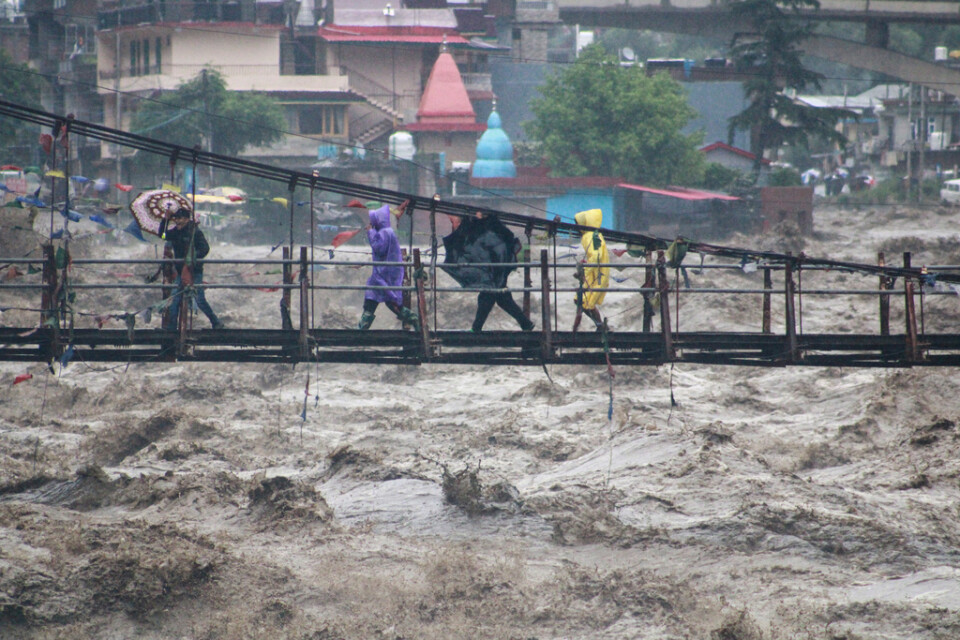 Människor på en bro över en översvämmad flod i den nordliga delstaten Himachal Pradesh i Indien.