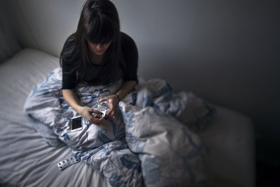 En ung kvinna sitter i en säng med en karta tabletter i handen. Detta är en genrebild till ämnet psykisk ohälsa, som många av de unga i Ulricehamn som inte studerar eller jobbar lider av.